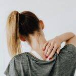 A woman in casual clothing holds her neck, indicating pain or discomfort.