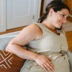 A joyful pregnant woman relaxing on a Pregnancy Pillow indoors, enjoying a book.