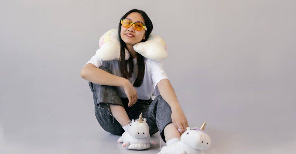 Smiling young woman wearing unicorn slippers and colorful sunglasses indoors with a relaxed pose.