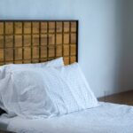 A stylish bedroom featuring a wooden headboard, wall lamp, and white bedding.
