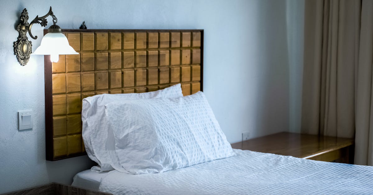 A stylish bedroom featuring a wooden headboard, wall lamp, and white bedding.